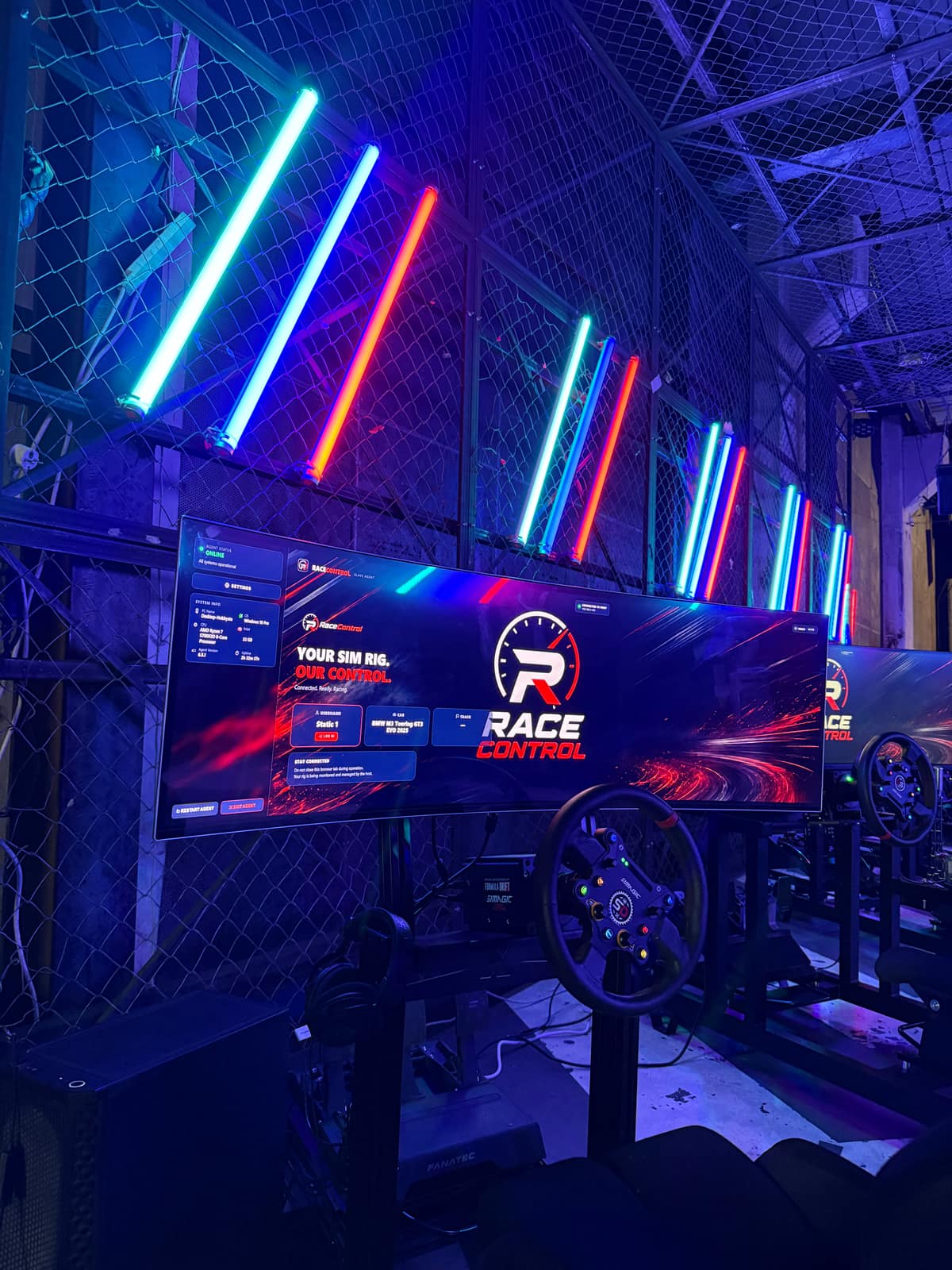 A simulator seat and wheel in front of an ultrawide screen showing the RaceControl idle display