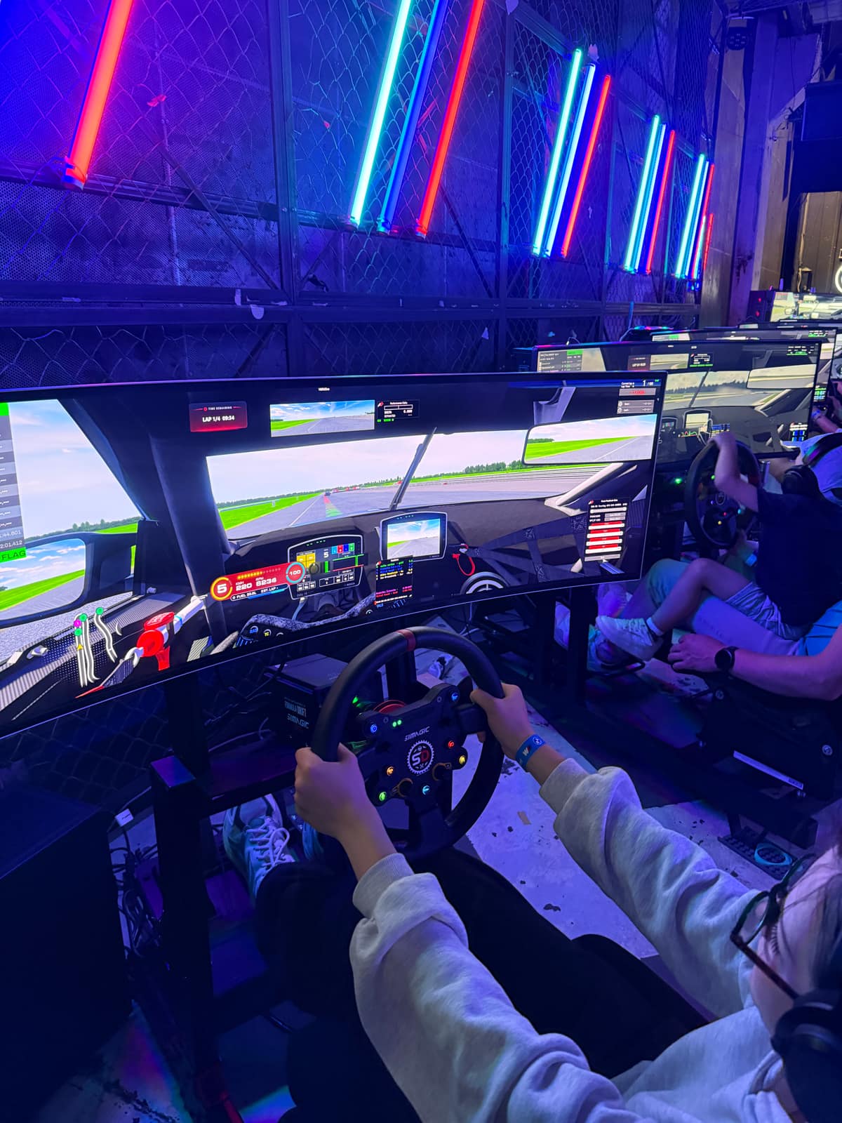 A driver's hands on the wheel with the track and timing on screen