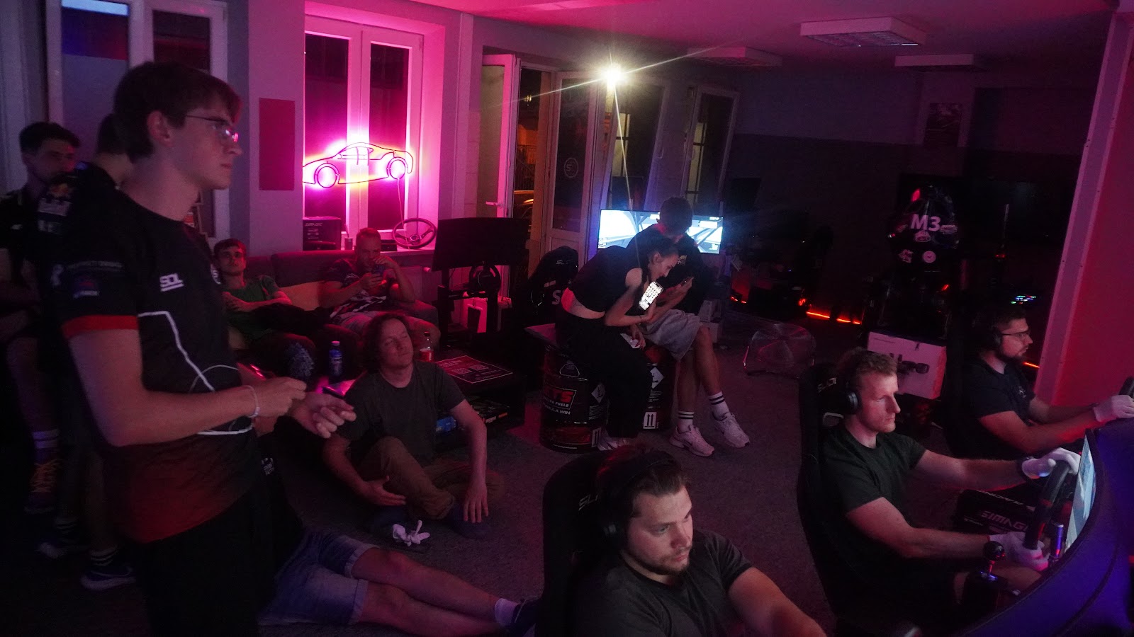 Wide view of the SimRacingDream room with the row of simulators occupied by league drivers under pink and blue lighting