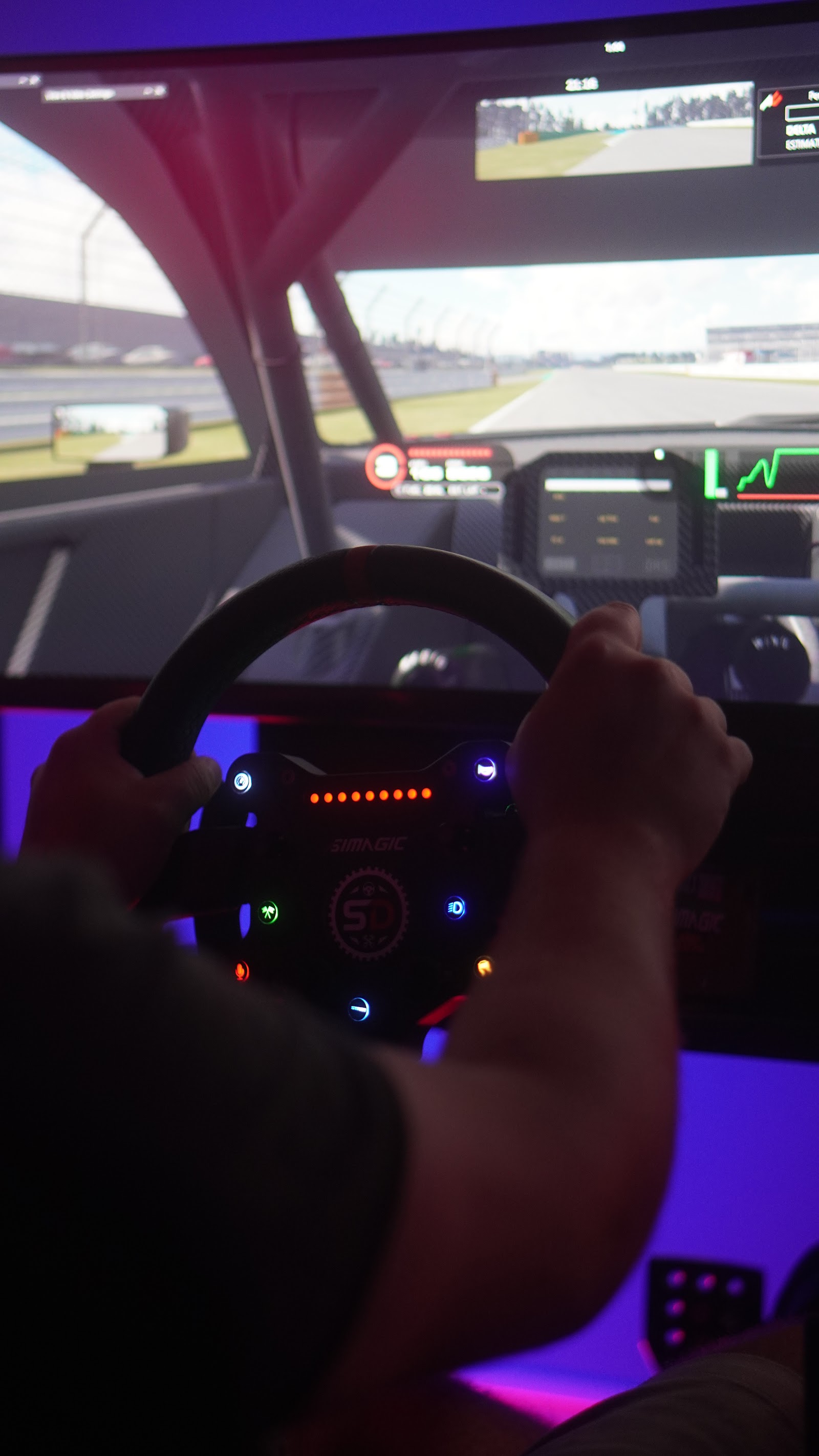 A driver's hands on the wheel of a simulator, the track on the screens ahead
