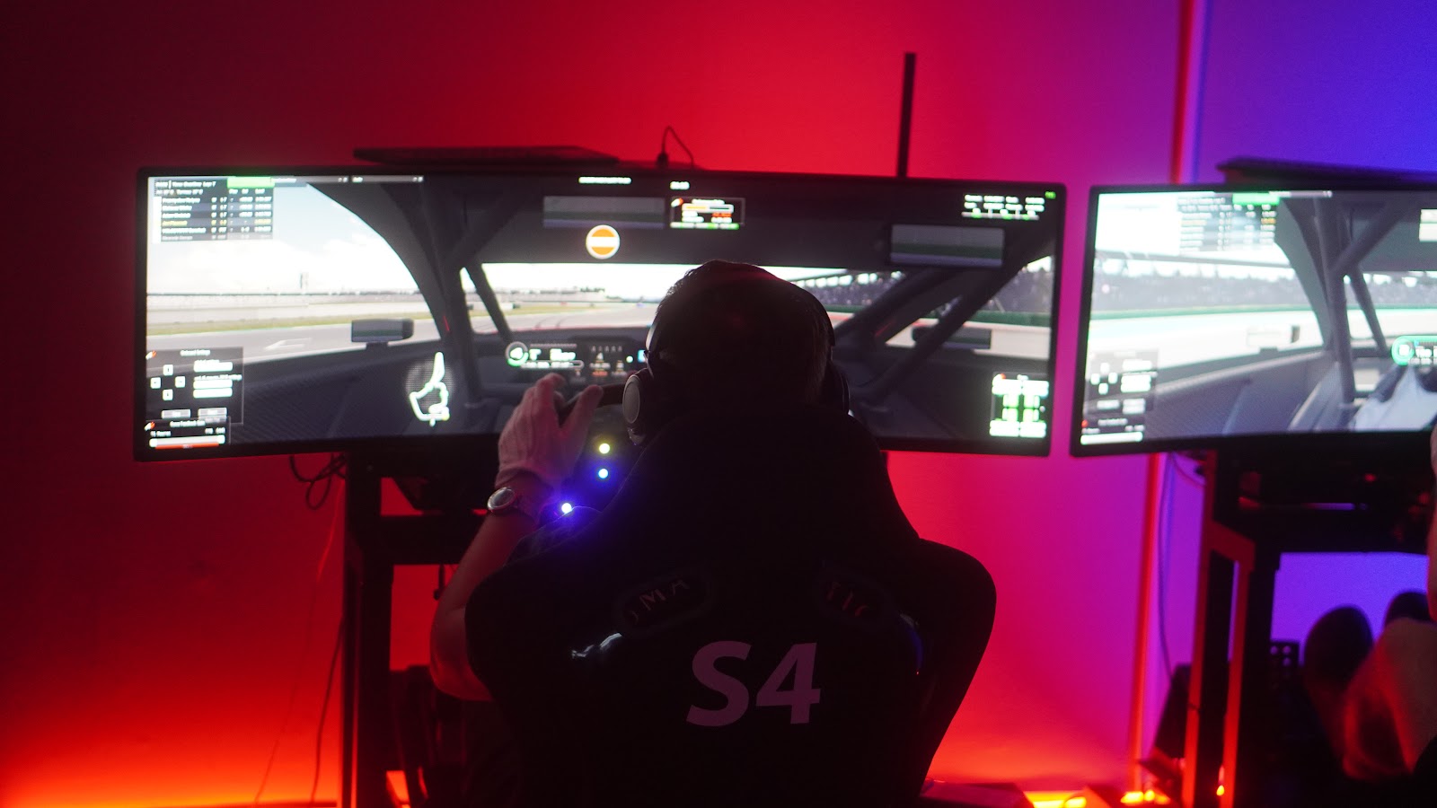 A simulator rig lit red, screens showing the race in progress